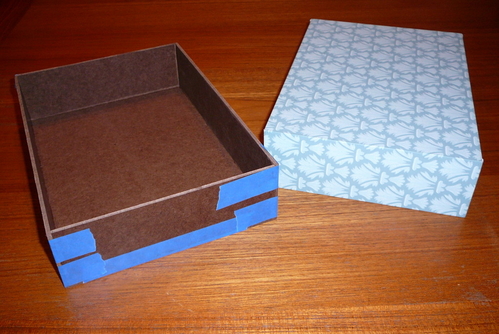 Hardboard Storage Boxes
I made some storage boxes for my workbench from tempered hardboard, 1/8-inch thick.  The first prototype (covered in wallpaper and flipped upside down) has two sides raised up so that the lid is partially inset (like a cigar box).  The second prototype, here being held together with blue masking tape while the glue dries will have a simpler full-overlay flip top.

Finished size of the box is 7-3/4 x 11 x 2-5/8 inches.  These are the same dimensions, except shorter, as the photo/video craft boxes made from cardboard that are sold in the US.

The joints are butted together, glued with carpenter's glue.  I applied a glue fillet to the inside and then ended up pasting on wallpaper to the outside of the first box.  I'll probably do the same with the others.
